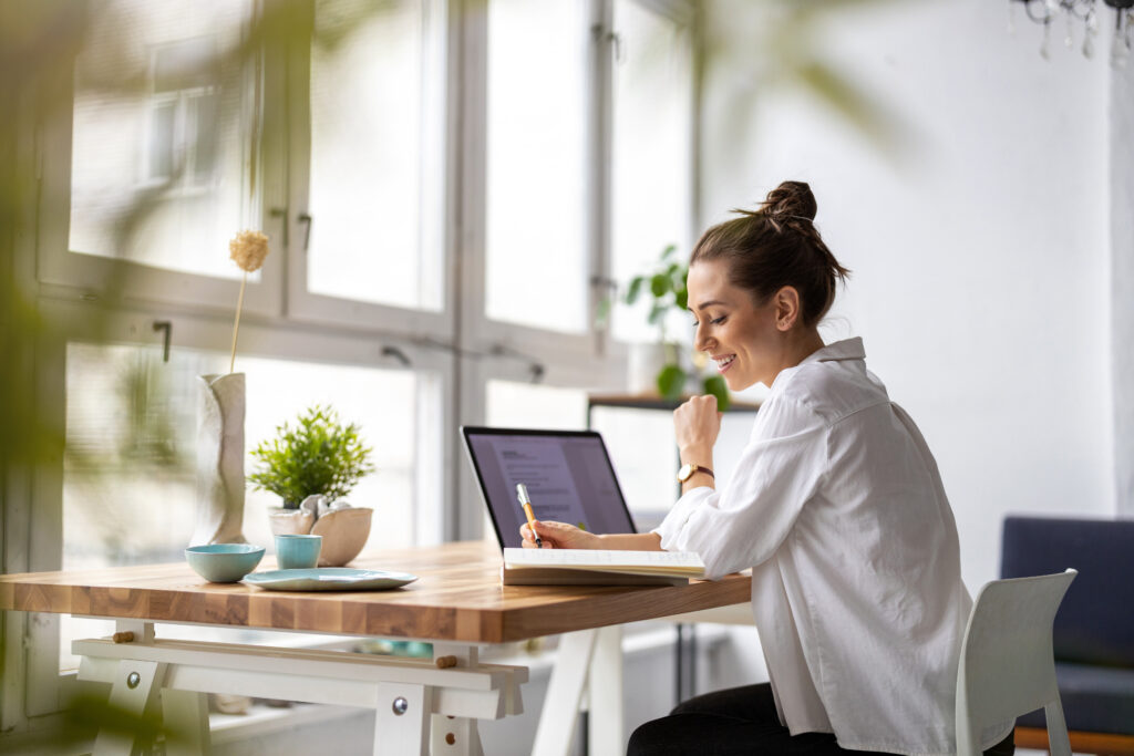 Smiling woman sitting at her desk, symbolizing the peace that comes from letting go of strain and embracing a more aligned, sustainable way of living.